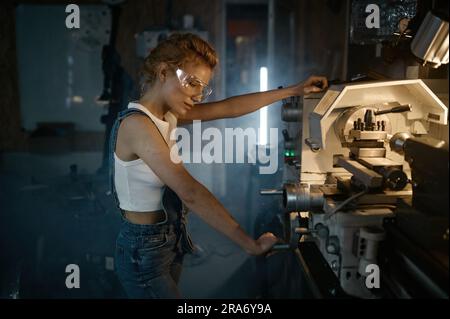 Giovane ingegnere meccanico bionda che lavora su una macchina da tornio Foto Stock