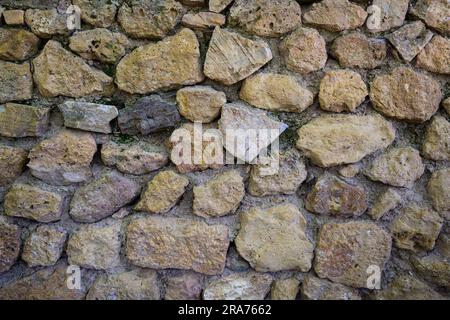 Vecchio muro panoramico grossolano in pietra fatto di varie pietre naturali quadrate in beige, ocra e marrone Foto Stock