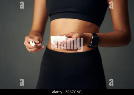Primo piano di una giovane donna birazziale che indossa un fitness tracker e che indossa cuffie intrauricolari wireless Foto Stock
