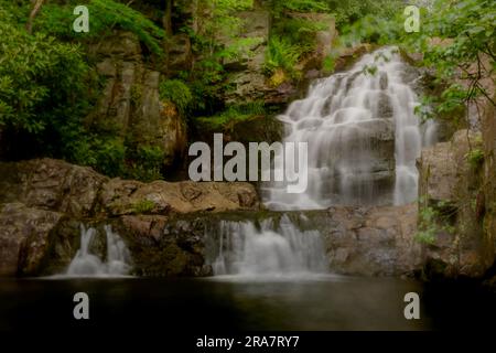 cascate che si infrangono sulle rocce fino alla piscina scura in un luogo appartato tra boschi circondati da verde vegetazione Foto Stock