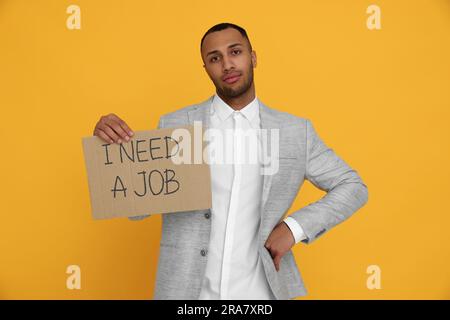 Giovane disoccupato con un cartello con la frase ho bisogno di Un lavoro su sfondo giallo Foto Stock