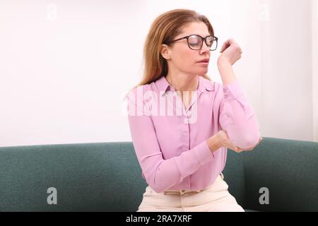 Donna che soffre di dolore al gomito al chiuso. Sintomi dell'artrite Foto Stock