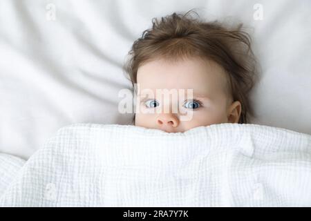 Piccolo e grazioso bambino sdraiato sotto la coperta su un letto morbido, vista dall'alto Foto Stock