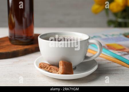 Tazza di caffè aromatico, caramelle al caramello e sciroppo su un tavolo di legno bianco Foto Stock