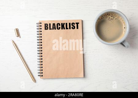 Lista nera di Word scritta in blocco note, penna e caffè su un tavolo di legno bianco, con letto piatto Foto Stock