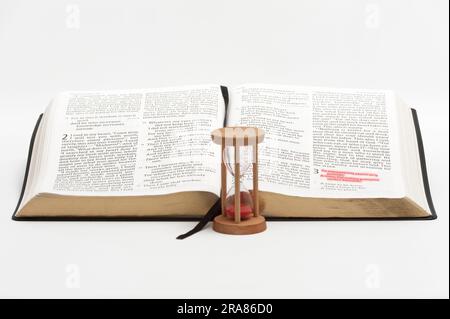 Clessidra e bibbia aperta sul libro degli Ecclesiasti con particolare attenzione al versetto 1 del capitolo 3 evidenziato in rosso. Isolato su sfondo bianco. Foto Stock
