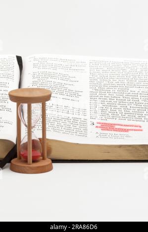 Clessidra e bibbia aperta sul libro degli Ecclesiasti con particolare attenzione al versetto 1 del capitolo 3 evidenziato in rosso. Isolato su sfondo bianco. Foto Stock