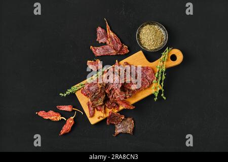 Vista dall'alto delle fette di agnello essiccate a strappi su un tagliere di legno con sale e pepe Foto Stock