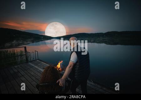 Coppia simpatica guarda il tramonto seduto accanto al fuoco sul molo, vista sul retro Foto Stock