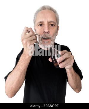 Un uomo maturo sta bevendo un cucchiaio di sciroppo per la tosse per curare il mal di gola e la bronchite. Isolato su sfondo bianco Foto Stock