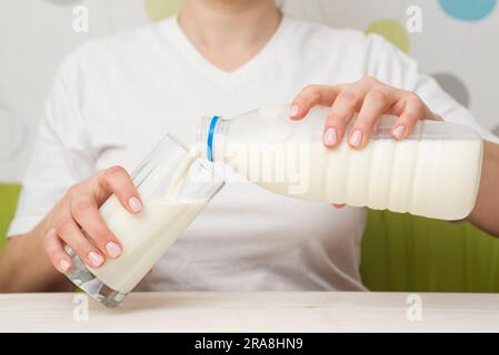 Una donna versa il latte da una bottiglia di plastica in un bicchiere. Dieta sana Foto Stock