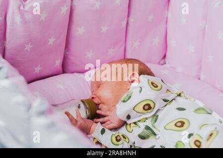 Un neonato beve autonomamente latte o una miscela secca da un biberon, a casa Foto Stock