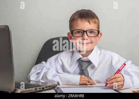 Un bambino adorabile sta lavorando su un computer portatile con abiti e occhiali. Foto Stock