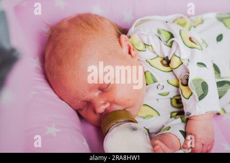 Un neonato beve autonomamente latte o una miscela secca da un biberon, a casa Foto Stock