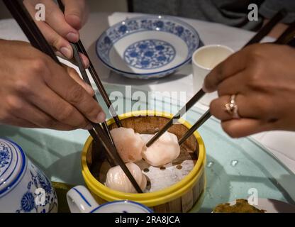 Yumcha, dim sum nel piroscafo di bambù. Mani che tengono le bacchette per gnocchi. Cucina cinese. Attenzione selettiva ai ravioli. Foto Stock