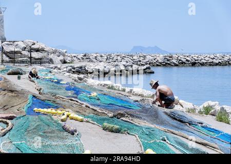 Due pescatori che riparano le loro reti da pesca sul lato del porto di pesca. Il porto si trova a Estepona, Spagna, con Gibilterra sullo sfondo Foto Stock