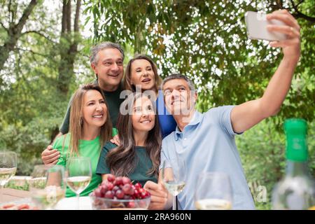 Gruppo di amici maturi che scattano selfie con lo smartphone e fanno barbecue all'aperto Foto Stock