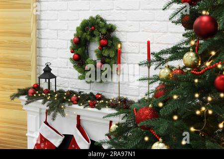 Splendida corona di Natale appesa sopra il caminetto vicino all'albero al chiuso Foto Stock