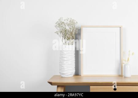 Cornice fotografica vuota, vasi con punte decorative asciutte e fiori di gitosfila su tavolo in legno. Mockup per il design Foto Stock