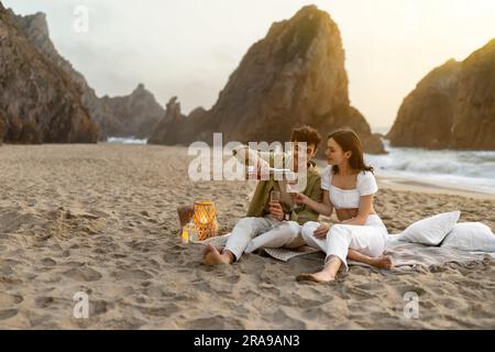 Una coppia europea che ama la bottiglia di vino, un romantico picnic sulla spiaggia vicino all'oceano, spazio libero Foto Stock