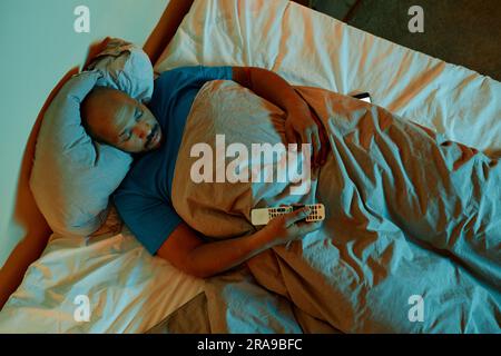 Vista dall'alto da un uomo nero che guarda la TV a letto di notte soffre di insonnia Foto Stock