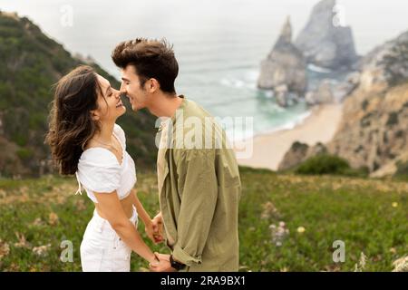 Felice giovane ragazzo europeo che si tiene per mano e si unisce, naso tuchigno, si gode la data sulla costa, spazio per copiare Foto Stock