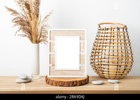 Decorazioni minimali in legno naturale con cornice bianca vuota, canne a secco in vaso e lanterna rotonda in legno a lume di candela. Sfondo interno casa. Foto Stock