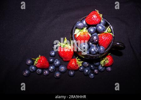 Composizione di un tè riempito di mirtilli e fragole viste direttamente dall'alto su sfondo nero Foto Stock