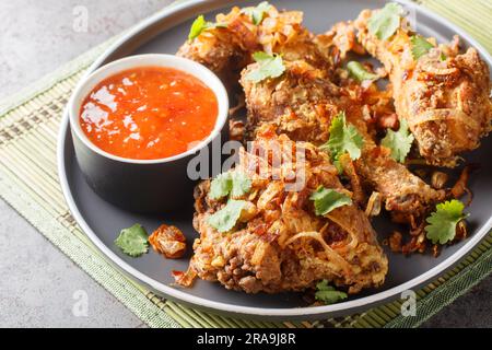 Pollo fritto Thailand Hat Yai con salsa dolce al peperoncino e cipolle croccanti da vicino su un piatto sul tavolo. Orizzontale Foto Stock