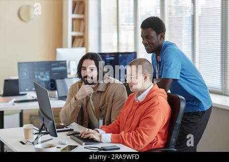 Giovane donna d'affari che digita sulla tastiera del computer mentre i suoi due colleghi interculturali maschi guardano lo schermo durante una riunione di lavoro Foto Stock
