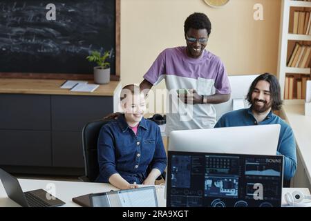 Gruppo di giovani e allegri responsabili IT che discutono di curiosi video online o di idee di lavoro mentre guardano lo schermo del computer Foto Stock