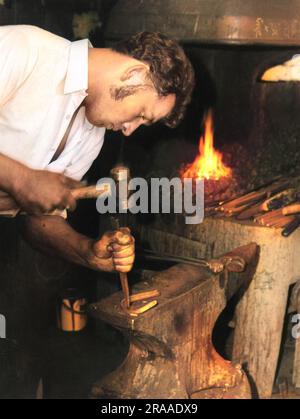 Un giovane contadino (fabbro) usa un martello e uno scalpello sulla sua incudine per formare un ferro di cavallo. Data: Anni '1960 Foto Stock