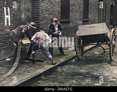 Fireman, A.R.P uomini e volontari si muovono per attaccare rapidamente un tubo all'idrante di pavimentazione più vicino a un incendio causato dalla campagna di bombardamento tedesco sulla capitale per tutto il 1940, noto come Blitz. Data: Circa 1940 Foto Stock