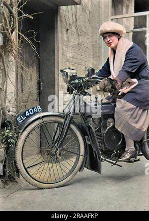 Una donna su una motocicletta Douglas a lato di una casa. Indossa un berretto grande e guanti enormi. Foto Stock