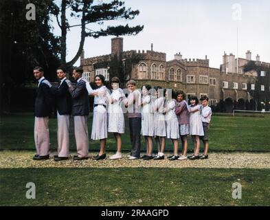 Dodici giovani in fila, dai più alti ai più piccoli, con un grande edificio sullo sfondo. Data: 1930 Foto Stock