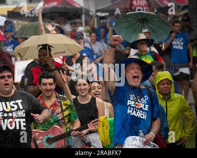 Piedi Lauderdale, Florida, USA. 2 luglio 2023. (Nota EDS lingua del corso, T-shirt a sinistra). La folla canta sotto la pioggia a un raduno prima della marcia We the People National a Fort Lauderdale, Florida. Quando la marcia stessa iniziò in una discesa torrenziale, la folla si era gonfiata a diverse migliaia di persone. La marcia fu messa in scena nel centro di Fort Lauderdale, in Florida, il 2 giugno 2023. L'evento si è concentrato sull'erosione della democrazia, sul controllo delle armi, e soprattutto in Florida, sui recenti attacchi alle libertà delle persone gay e transgender. La protesta è stata organizzata dalla Fondazione AIDS Healthcare Foto Stock