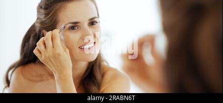 Felice giovane donna sagomare le sopracciglia in bagno Foto Stock