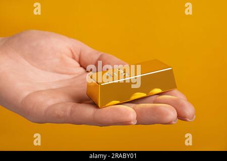 Donna che tiene la barra d'oro su sfondo arancione, primo piano Foto Stock