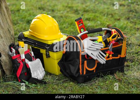 Borsa, cinghia e scatola con diversi attrezzi per la riparazione sull'erba vicino agli alberi all'esterno Foto Stock