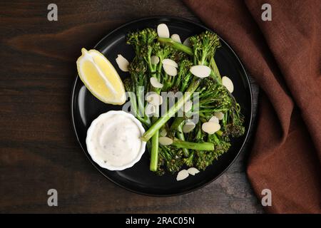 Gustosi broccolini cotti con mandorle, limone e salsa su un tavolo di legno, vista dall'alto Foto Stock