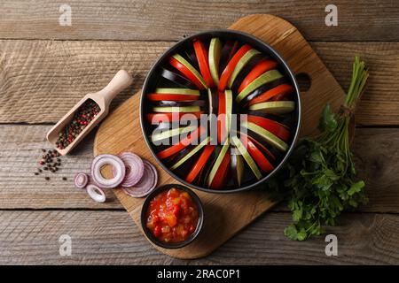 Cucinare una deliziosa ratatouille. Verdure fresche diverse, paletta con spezie e teglia da forno rotonda su un tavolo di legno, piatto Foto Stock