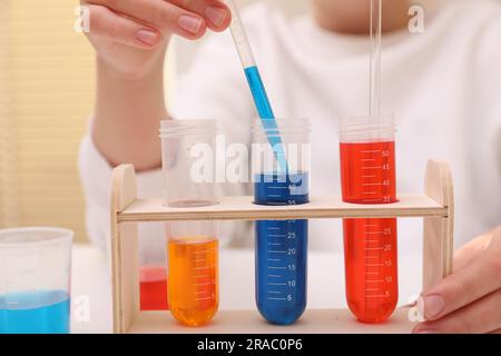 Ragazza che mescola liquidi colorati al tavolo bianco in interni, primo piano. Set di esperimenti chimici per bambini Foto Stock