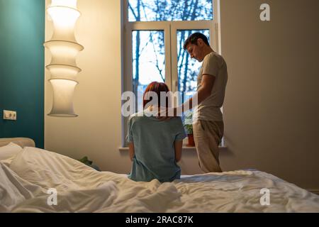 Supporto familiare. Una donna triste si siede sul letto vicino a un uomo in piedi, amorevole, marito che tocca la spalla della moglie Foto Stock