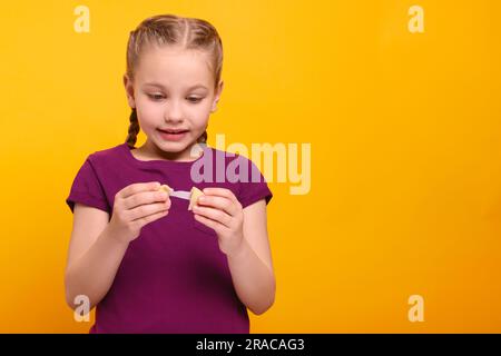 Ragazza carina che tiene un gustoso biscotto della fortuna e legge la previsione su sfondo arancione. Spazio per il testo Foto Stock