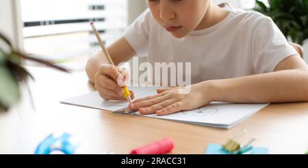 Un ragazzo carino crea un disegno con un righello e una matita. Lezioni a casa. Geometria e disegno. Foto Stock
