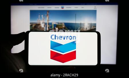 Persona che tiene il cellulare con il logo della società americana di energia Chevron Corporation sullo schermo davanti alla pagina Web aziendale. Concentrarsi sul display del telefono. Foto Stock