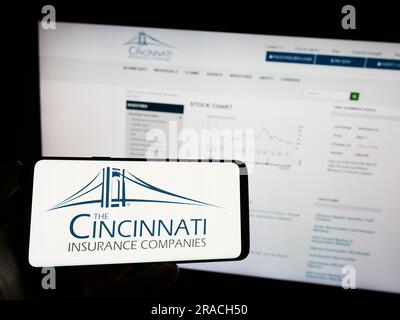 Persona che possiede un telefono cellulare con il logo della società statunitense Cincinnati Financial Corporation sullo schermo davanti alla pagina Web. Concentrarsi sul display del telefono. Foto Stock