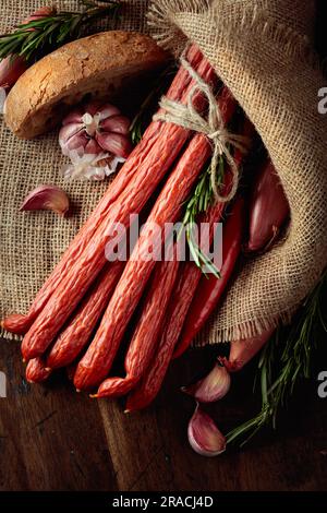 Salsicce affumicate con cipolla, aglio, pepe e rosmarino su un vecchio tavolo di legno. Vista dall'alto. Foto Stock