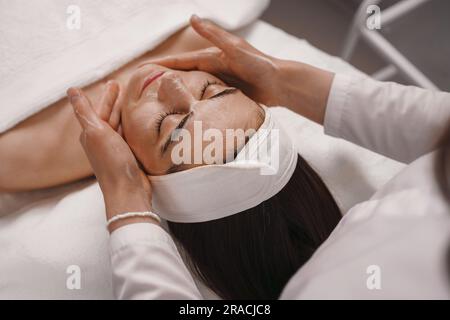 Massaggiatrice che fa un massaggio facciale ai clienti in una spa Foto Stock