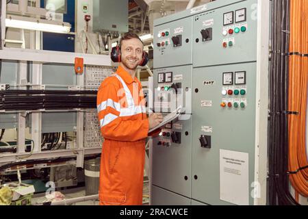 Giovane ingegnere professionista del settore petrolifero e del gas che controlla i parametri della scheda di commutazione ad alta tensione. Controlli di sorveglianza da parte dell'ingegnere marino. Foto Stock